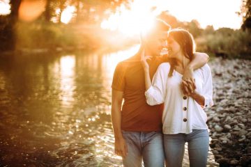 Boyfriend and girlfriend walking near river on summer day, holding hands, embracing