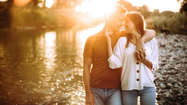 Boyfriend and girlfriend walking near river on summer day, holding hands, embracing